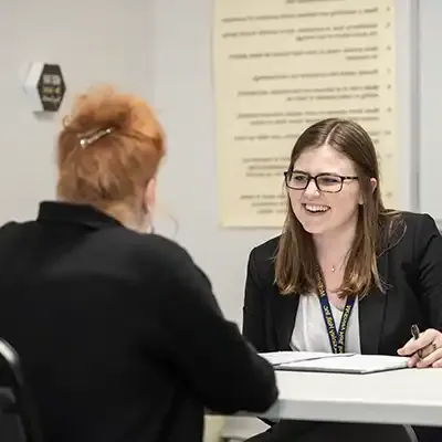 Two females seated at a table discussing an issue, notes are being recorded in a notebook.