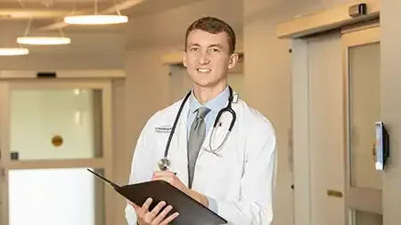 Male phamacy student wearing a stethoscope taking notes.