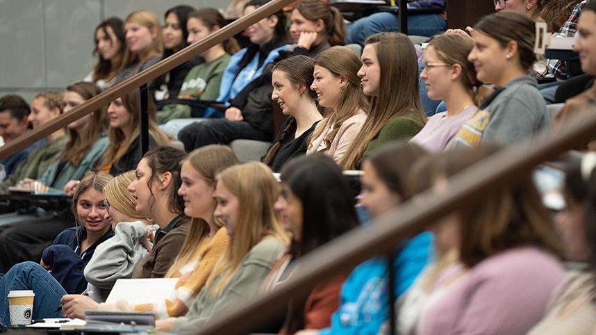 Smiling students sitting in class in the Scharnberg Business and Communication Center auditorium.