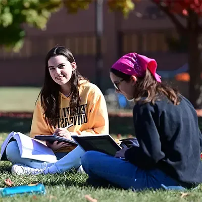 Female students sitting on the lawn studying outside on a sunny day.